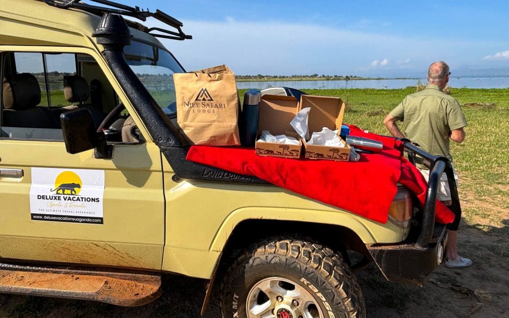 Guest enjoying a safari picnic beside a Deluxe Vacations Uganda vehicle during a wildlife safari in Uganda