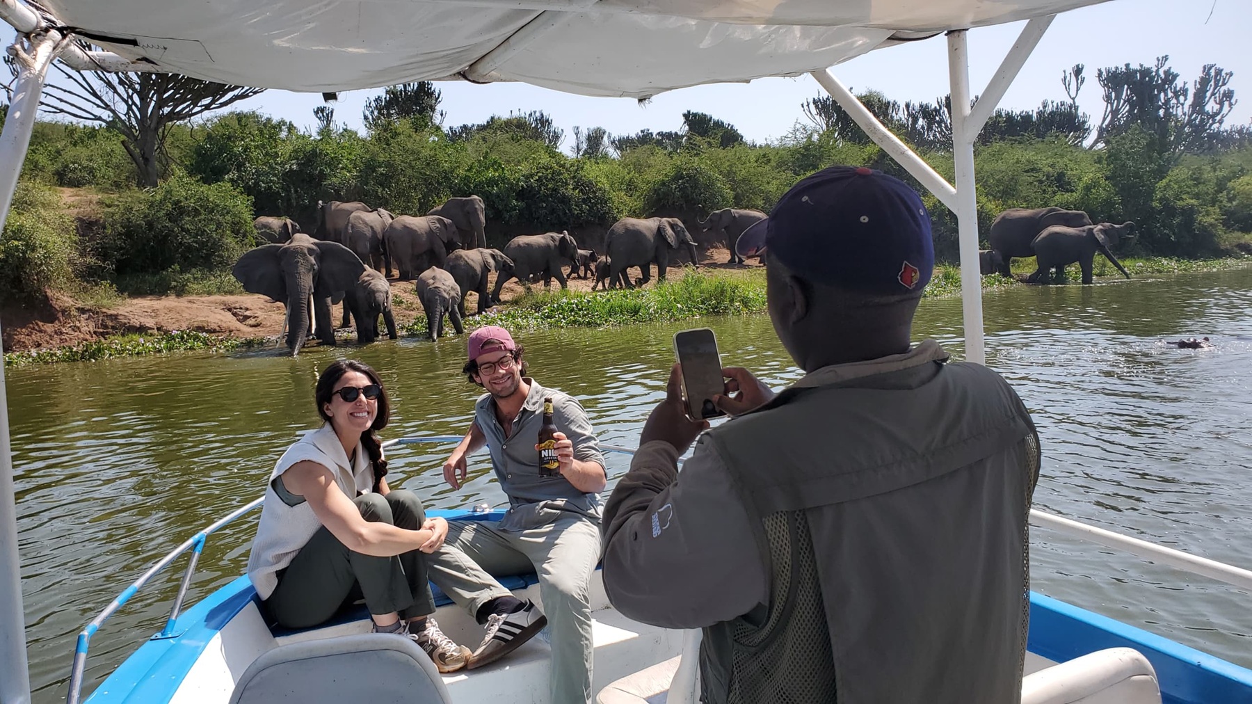 Visitors enjoying a private boat cruise on the Kazinga Channel with elephants on the shoreline in Queen Elizabeth National Park